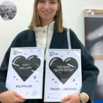 This image highlights a celebratory moment at ArtVilnius 2024, showcasing the awards for “Top 7 Gallery” presented to Wildpalms and “The Best Young Artist” awarded to Rachel Libeskind. Alexandra Meffert with the awards and behind Rachel's work