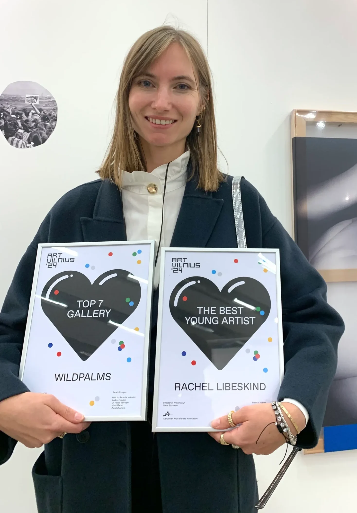 This image highlights a celebratory moment at ArtVilnius 2024, showcasing the awards for “Top 7 Gallery” presented to Wildpalms and “The Best Young Artist” awarded to Rachel Libeskind. Alexandra Meffert with the awards and behind Rachel's work