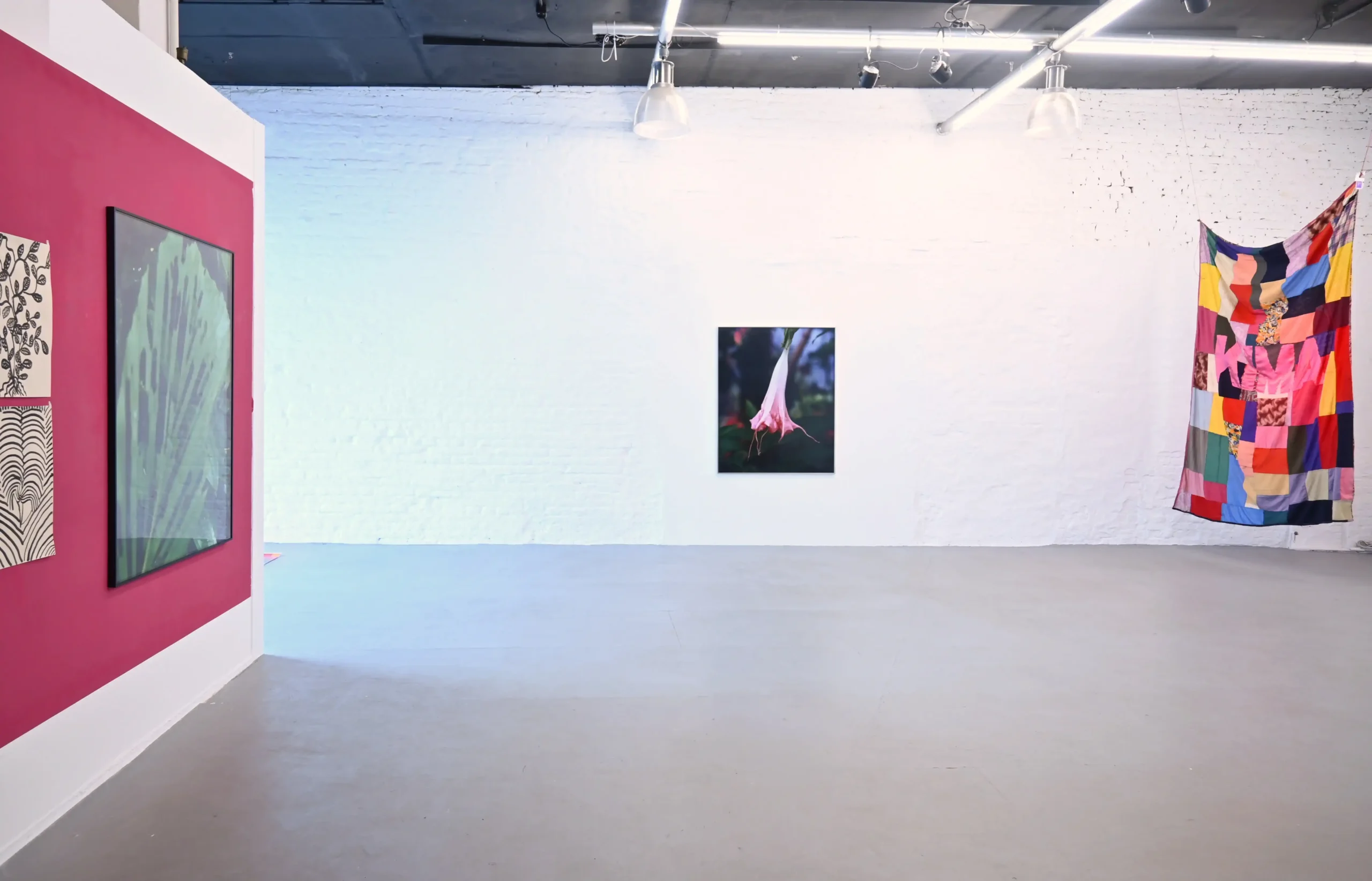 Wide KIMA exhibition view at wildpalms with photography, a colorful textile work, and geometric artwork