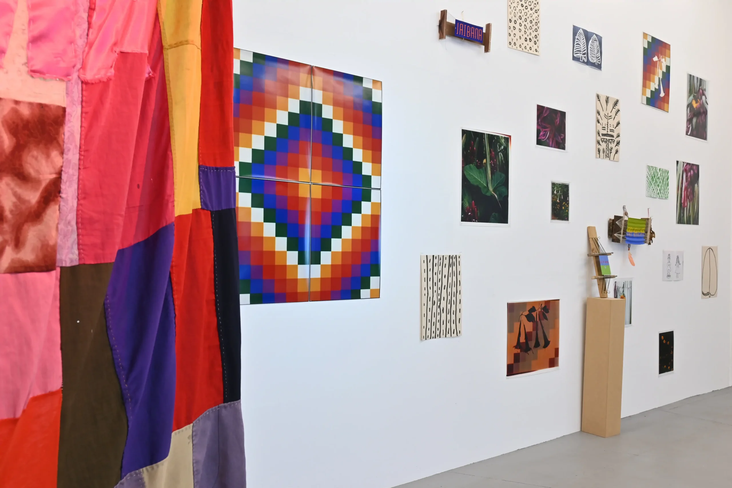KIMA exhibition view showing a colorful textile and a gallery wall of photographs, drawings, and woven works