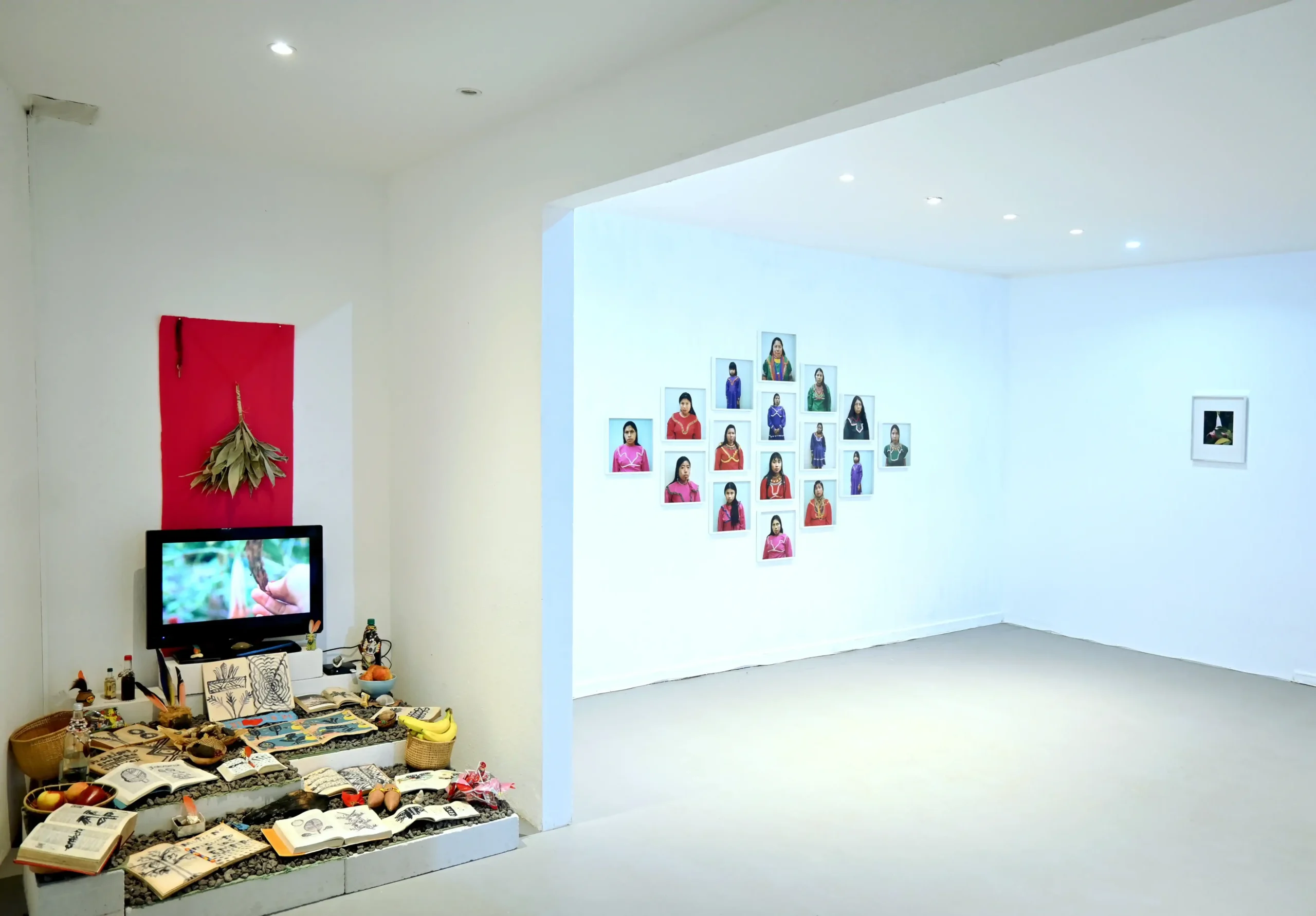 KIMA exhibition view with an altar and video installation beside a wall-mounted arrangement of portraits