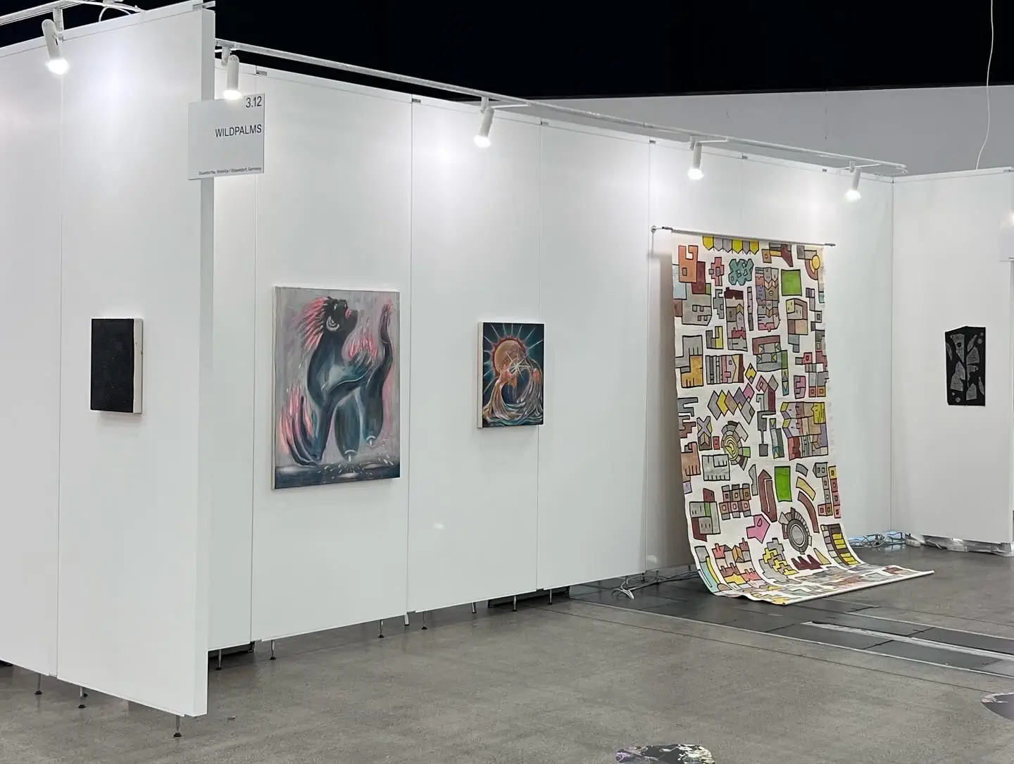 Vista del stand de wildpalms en ArtVilnius 2024 con pinturas y una gran obra colgante estampada