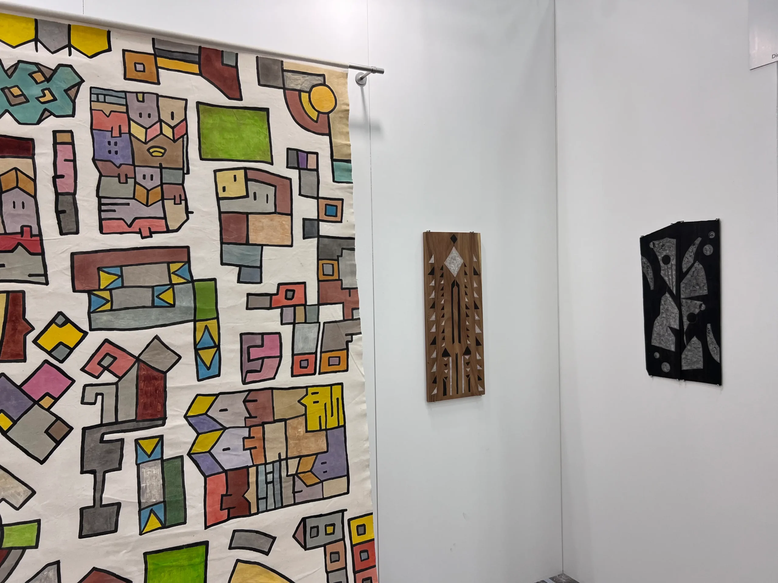 Detalle de una gran obra colgante estampada y multicolor junto a dos obras geométricas en madera en el stand de wildpalms