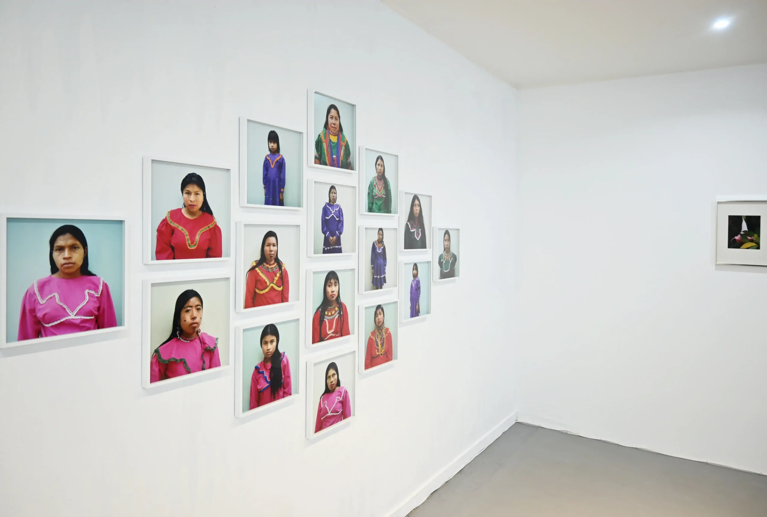 Angled KIMA exhibition view of Jepa, sixteen framed portraits of Emberá women, beside an Iguaka photograph
