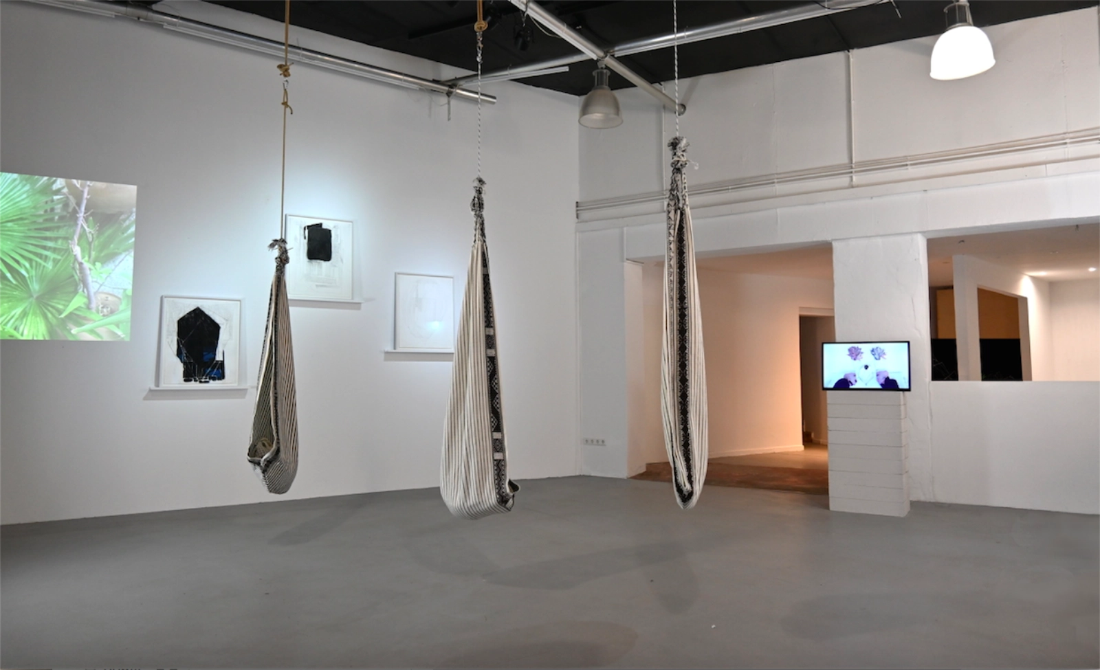 Magical Operations exhibition view with video projection, framed works and woven hanging seats