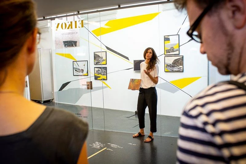 Inauguración de Babel: Tomorrow Was Another Day en el EIKON Schaufenster, Viena: una ponente se dirige al público frente a la instalación de Anibal Catalan.