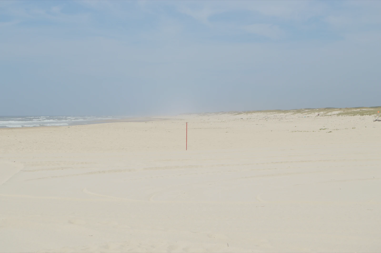 Mario Asef, Cenit, fotograma de vídeo de una playa con una vara roja delgada que no proyecta sombra