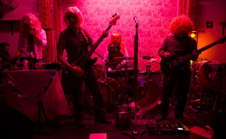La Rubia Te Besa actuando en directo bajo luz rosa, con los integrantes de la banda con pelucas rubias
