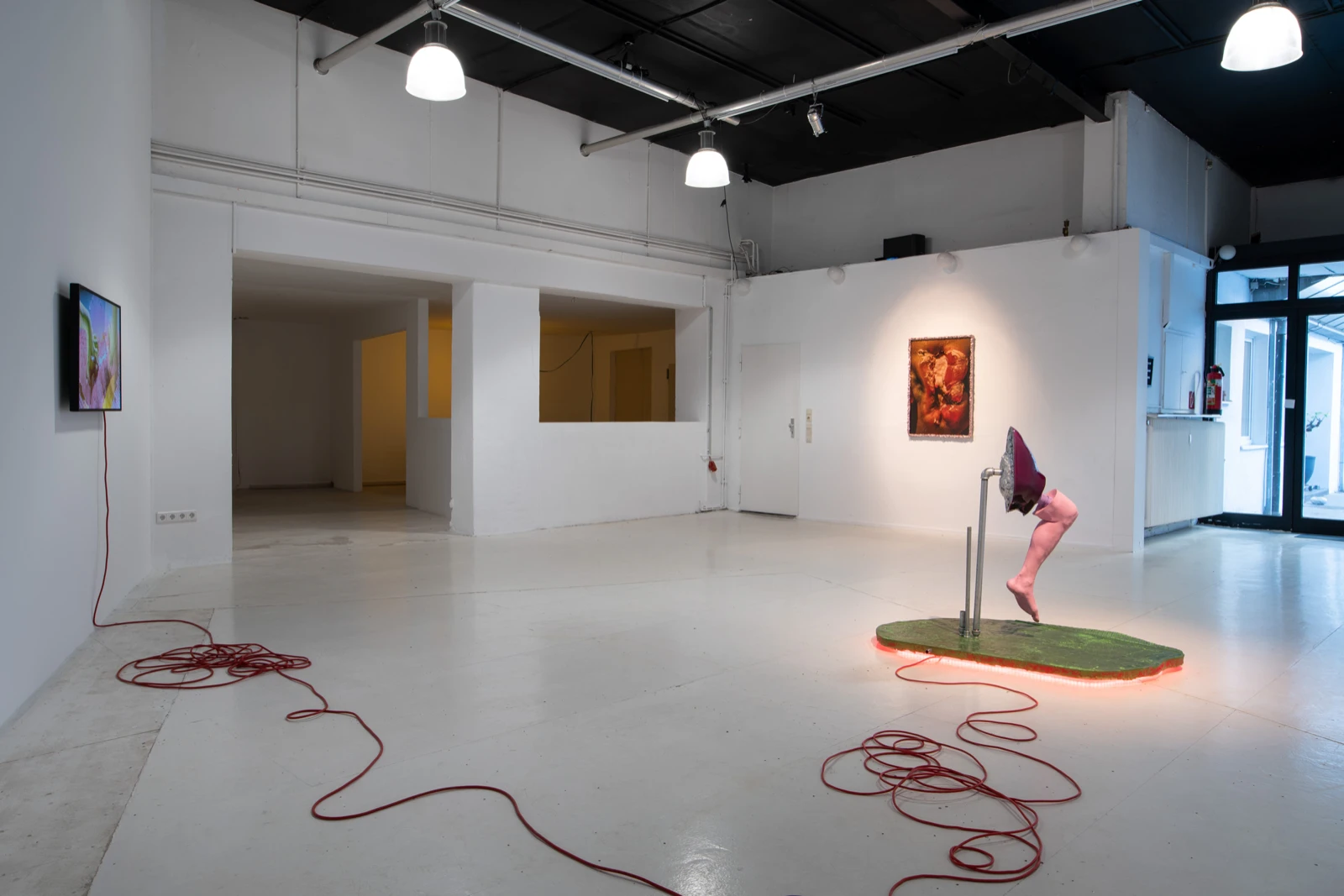 Vista del espacio de wildpalms durante Motherboard: la obra de video de Malte Bruns en la pared izquierda, una impresión enmarcada y la escultura sobre su plataforma iluminada.