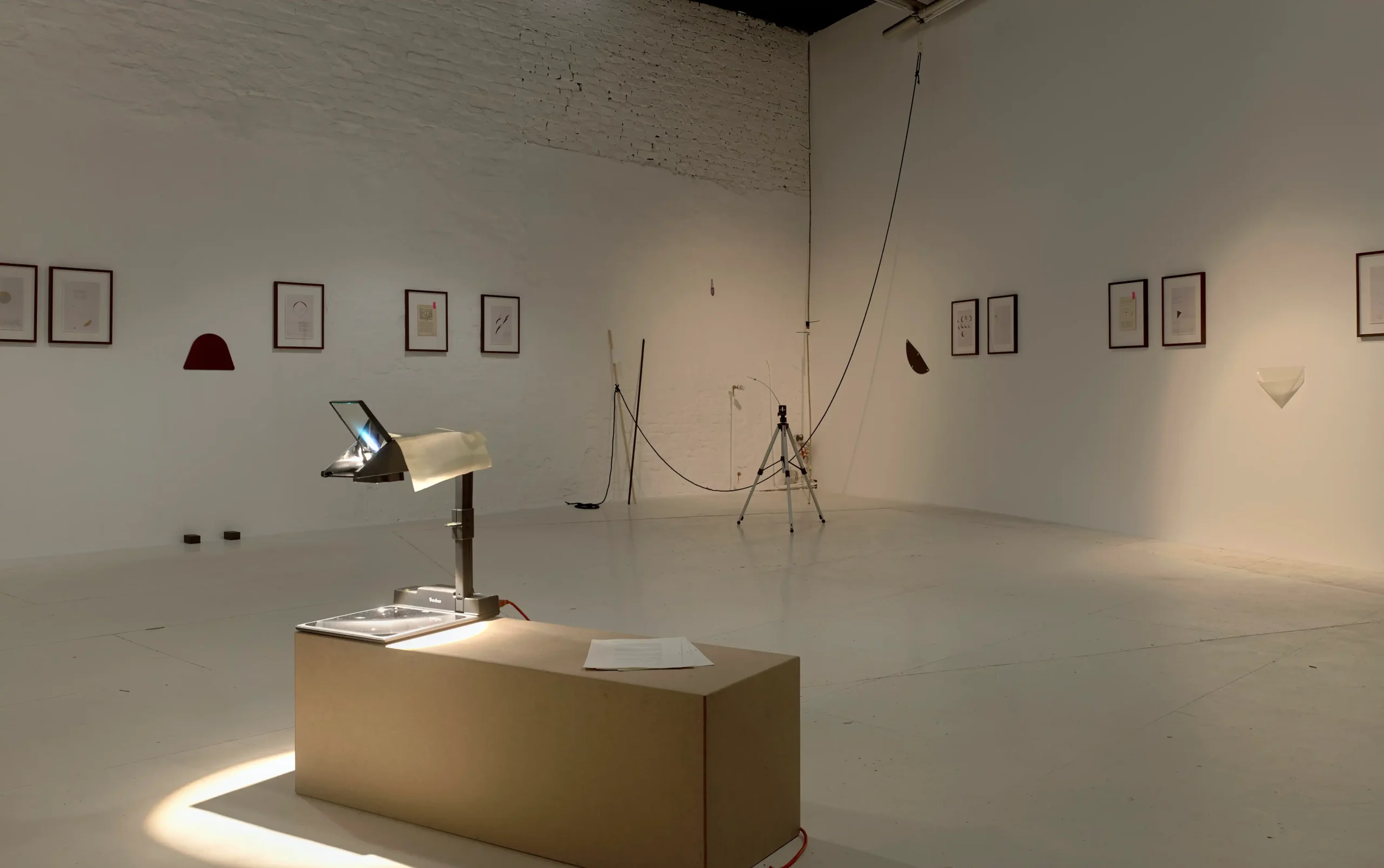 Mario Asef, Cenit, vista de instalación en wildpalms Düsseldorf con un retroproyector, obras enmarcadas y pequeñas esculturas en el suelo