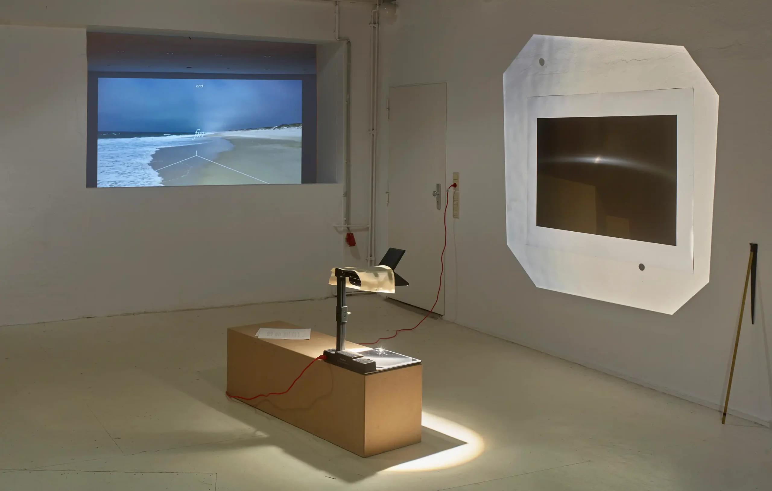 Mario Asef, Cenit, vista de instalación en wildpalms Düsseldorf con un vídeo de una playa que termina en «fin/end» y un monitor de pared con una luz dentro de una gran tela