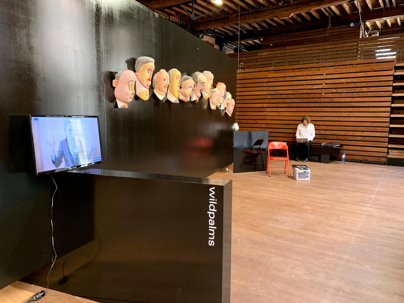 Vista general del stand de wildpalms con la fila de máscaras de madera de Mauricio Limón, una pantalla de video y área de asientos, POPPOSITIONS Art Fair, Bruselas
