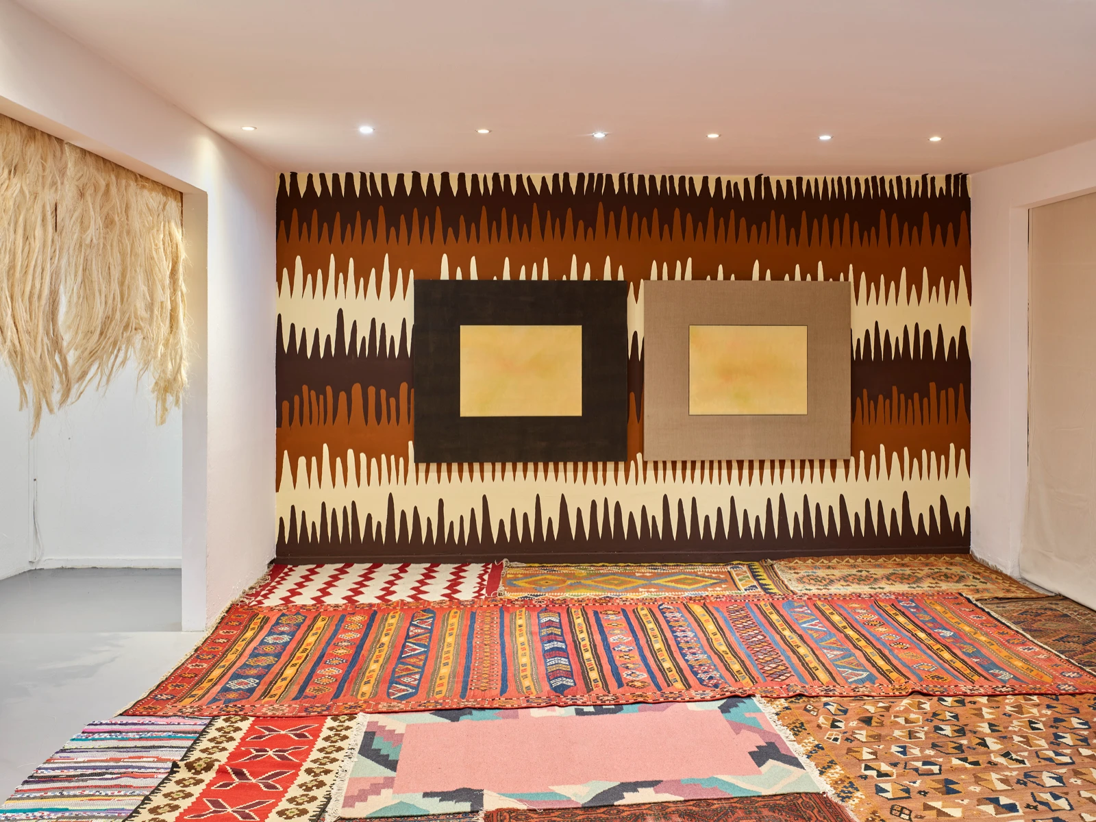 Dos pinturas de Mauricio Limón sobre una pared estampada, con el suelo cubierto de alfombras kilim, vista de instalación en wildpalms