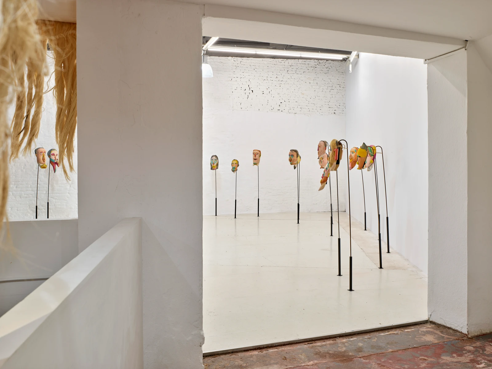 Vista a través de una puerta hacia las máscaras de madera pintadas de Mauricio Limón montadas en varillas en wildpalms