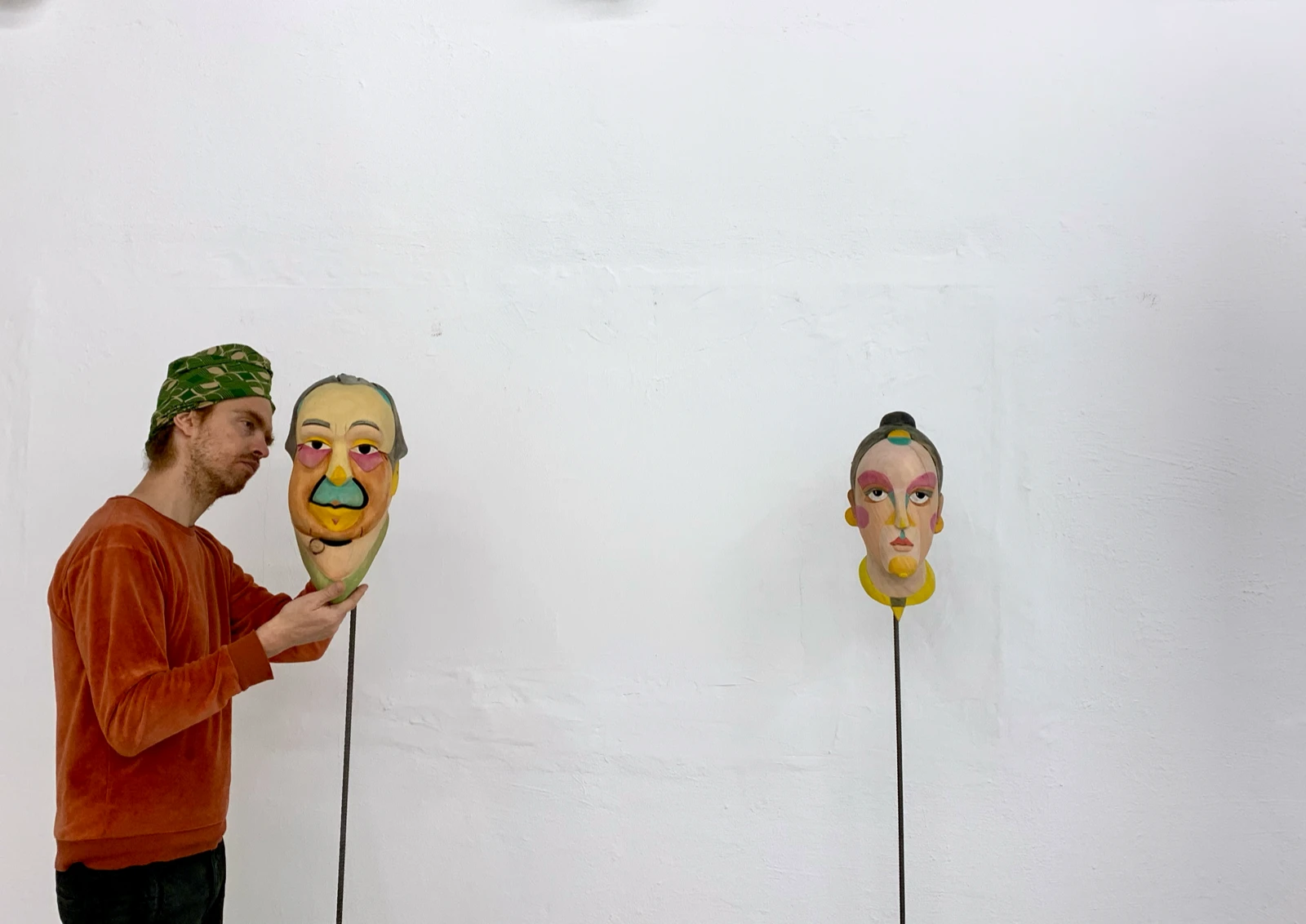 Una persona sosteniendo una de las máscaras de madera pintadas de Mauricio Limón junto a otra máscara montada en wildpalms